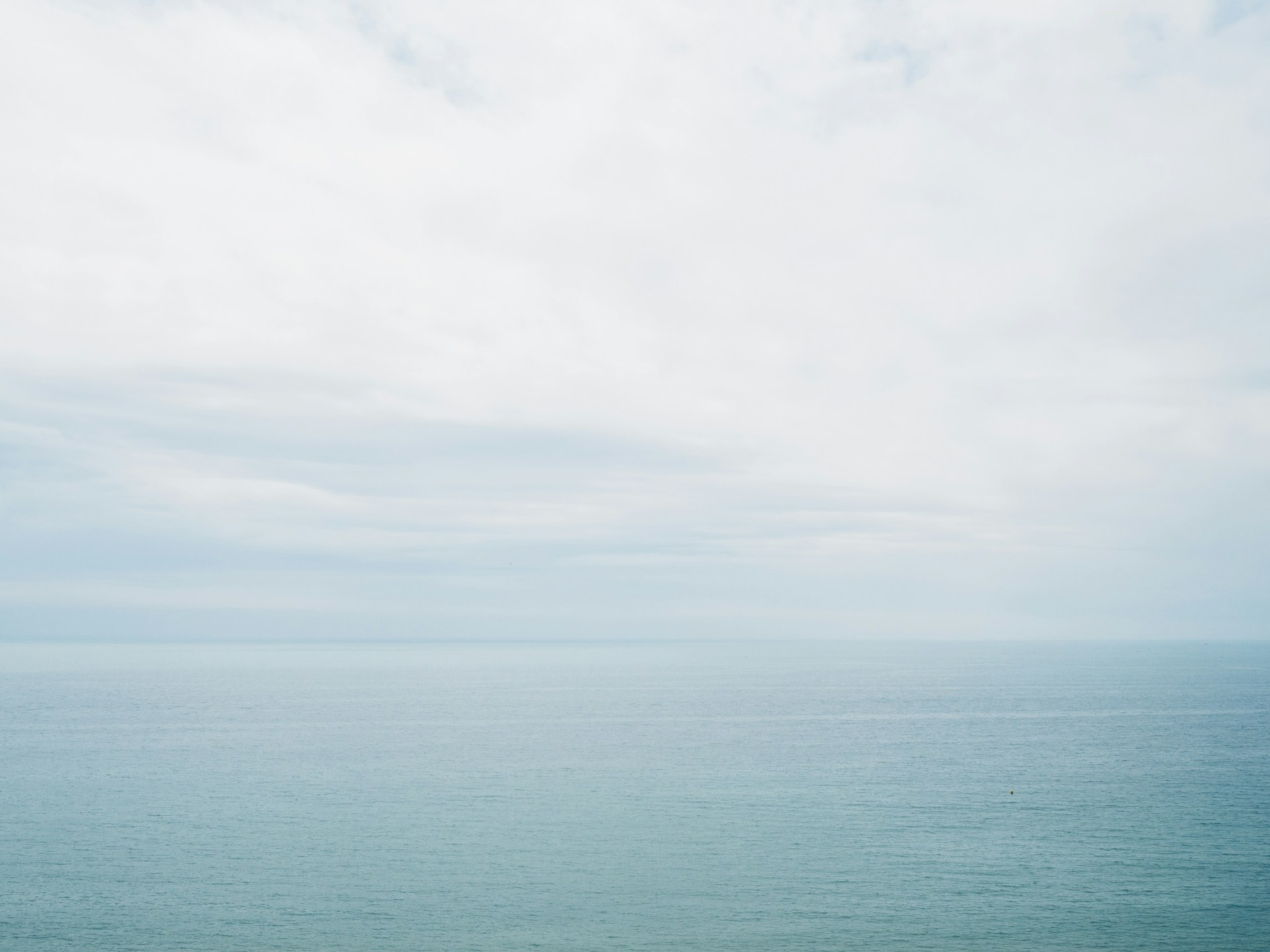 image of ocean horizon; the ocean is a teal color and the sky is cloudy and white